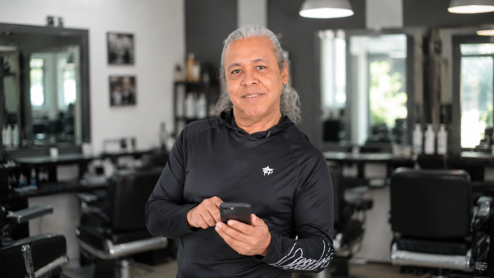 Hombre de 62 años con pelo canoso sonriendo en peluquería con smartphone en mano